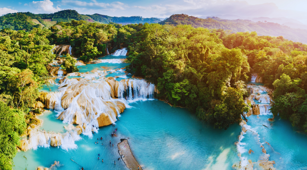 Aerial view of Agua Azul waterfalls in Chiapas, Mexico, with bright blue waters cascading through lush greenery.