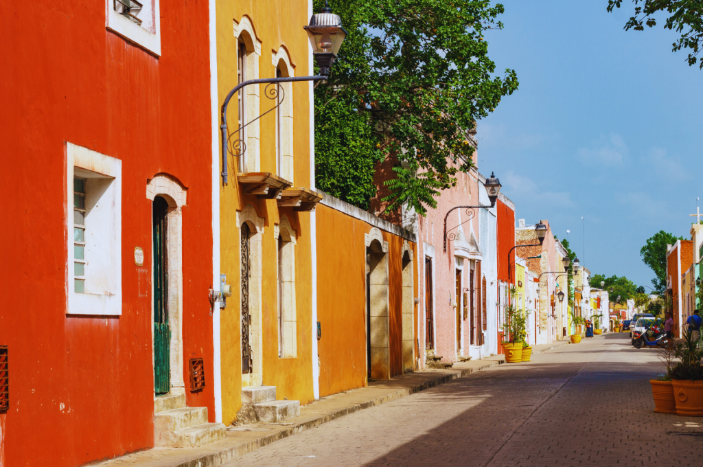 A perspective view of a colonial street in Valladolid, Mexico, with colorful red, yellow, orange facades of houses along the street.