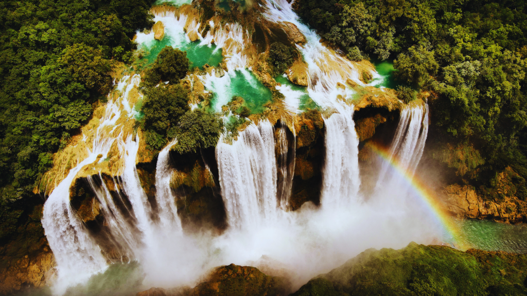 Aerial view of Tamul Waterfall in Mexico, with cascading waters, lush greenery, and a vibrant rainbow.