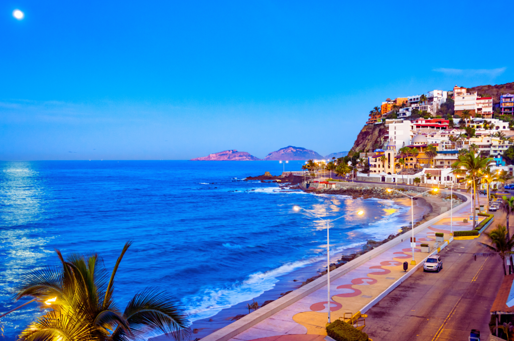 Scenic view of the Mazatlan coastline at dusk with the Pacific Ocean and illuminated beachfront walkway.
