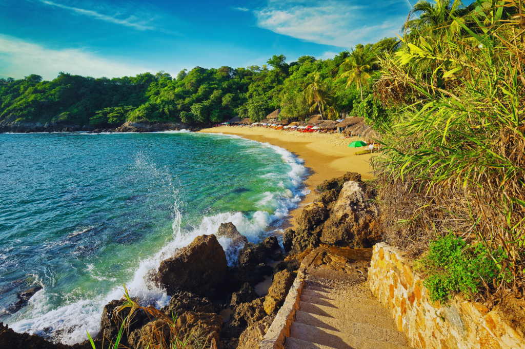 Scenic view of Playa Carrizalillo in Puerto Escondido, Mexico, with clear blue waters, golden sand, and lush greenery.