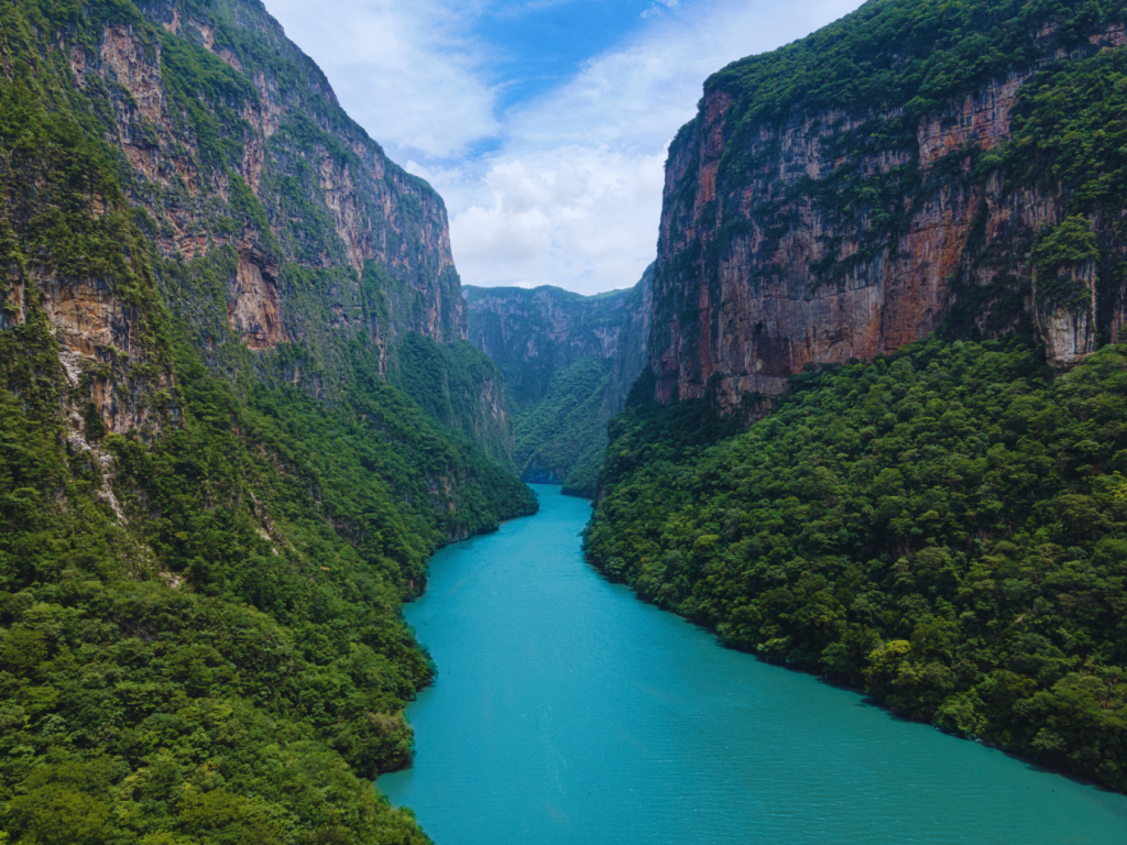 Aerial view of Sumidero Canyon in Chiapas, Mexico, with towering cliffs and a turquoise river flowing through the lush greenery.