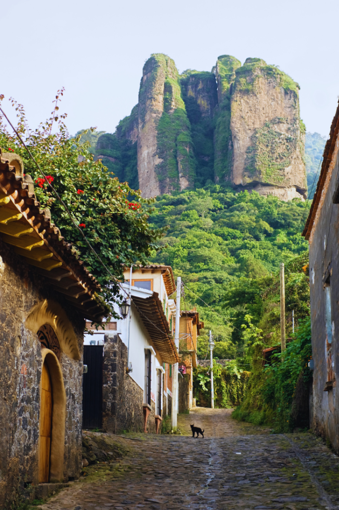 Cobblestone street in Tepoztlán, Morelos, with lush greenery and towering rock formations in the background.